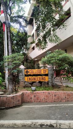 a yellow sign that reads college of engineering in front of a brick wall and trees