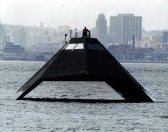 two people are standing on top of a boat in the water with buildings in the background