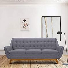 a living room with white walls and wooden floors, a gray couch in front of a painting on the wall