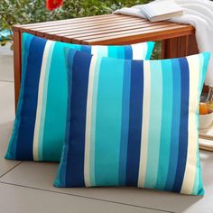 two blue and white striped pillows sitting on top of a wooden bench next to a potted plant