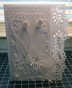 a white card with an intricate design on the front and side, sitting on a table next to a window