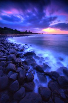 a painting of the ocean and rocks under a cloudy sky at night with purple clouds