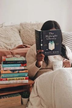 a woman sitting on a couch holding a book in her hands and reading it to the camera