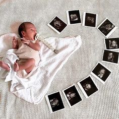 a baby laying on top of a white blanket next to many black and white photos