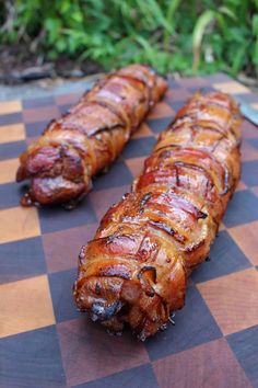 two bacon wrapped hot dogs sitting on top of a cutting board