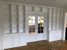 an empty living room with white bookcases and wood flooring, along with a dog laying on the floor