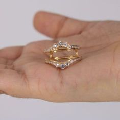 a person's hand holding a gold ring with three diamonds on top and bottom