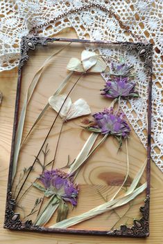 dried flowers are arranged in an old frame on a lace doily, with crocheted doily behind them