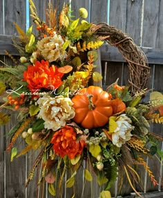 a wreath decorated with flowers and pumpkins on top of a wooden bench in front of a fence