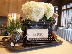 there is a typewriter with flowers on it and a happy sign in front of it