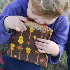 a little boy that is sitting down with a sandwich in his hand and some kind of bag