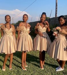 four beautiful young women standing next to each other on a grass covered field with flowers in their hands