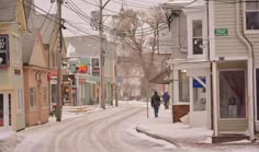 a person walking down a snowy street in front of some buildings and telephone poles with power lines above them