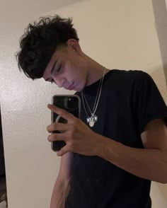 a young man looking at his cell phone while wearing a black t - shirt and silver necklace