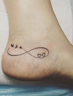 a tattoo on the foot of a woman with two birds flying over an infinite heart