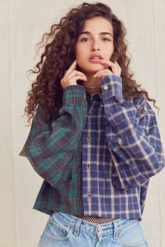 a woman with curly hair wearing a blue and green checkered shirt posing for the camera