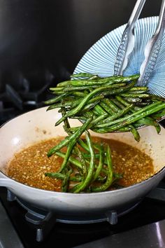 some green beans are being cooked in a pan on the stove top with tongs