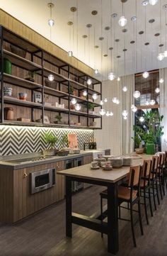 a dining room table and chairs with lights hanging from the ceiling above it, along with shelves filled with potted plants