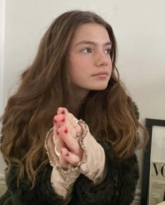 a woman with long hair holding her hand up to the side and looking off into the distance