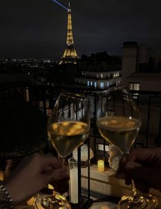 two people toasting with wine glasses in front of the eiffel tower at night