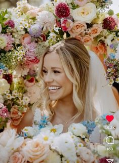 a woman in a wedding dress surrounded by flowers and greenery smiling at the camera