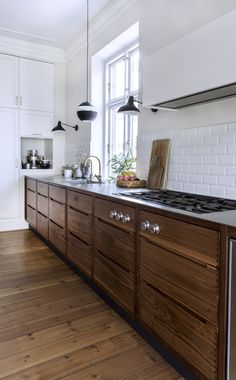 a kitchen with wooden cabinets and white walls, an island countertop and two hanging lights