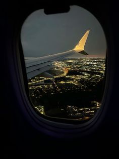 an airplane wing seen through the window of another plane at night with city lights in the background