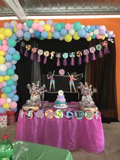 a table topped with balloons and cake next to a volley ball goal covered in tassels