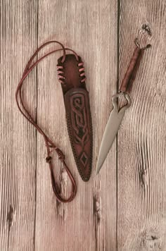 a knife and sheath laying on top of a wooden table next to a corded pocket knife