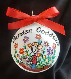 a white ornament with a red ribbon around it that reads garden goddesss