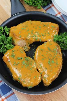 two pieces of chicken covered in gravy and garnished with parsley