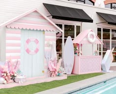 a pink and white beach hut next to a swimming pool with surfboards on it