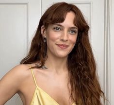 a woman with long hair wearing a yellow dress and smiling at the camera while standing in front of a white door