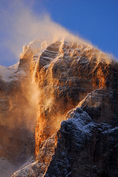 the sun is shining on some snow covered mountain peaks in the distance, with steam rising from them