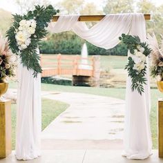 an outdoor wedding ceremony with white drapes and flowers on the arch, along with gold vases