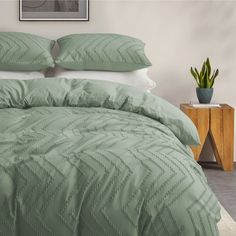 a bed with green comforter and pillows in a room next to a potted plant