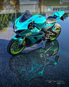 a blue and green motorcycle parked on top of a wet parking lot next to a fence