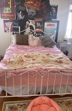 a bed with pink sheets and pillows in a room full of posters on the wall