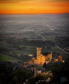 an aerial view of a town at night with the sun setting in the distance and lights on