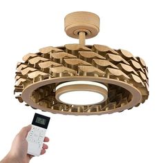 a hand holding a remote control in front of a light fixture made out of wood