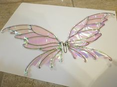 a butterfly made out of plastic sitting on top of a piece of white paper next to a tile floor