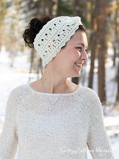 a woman wearing a white knitted headband in the snow with trees behind her