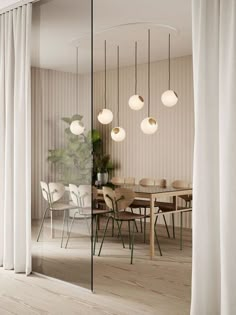 a dining room table with chairs and lights hanging from it's ceiling, next to a glass wall