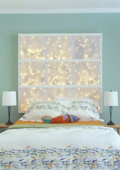 a bed that has some lights on the headboard and pillows in front of it