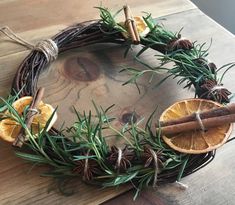 an orange and rosemary wreath on a wooden table with cinnamon sticks, pine cones and cinnamons