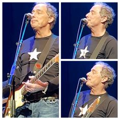 the man is playing his guitar and singing into some microphones while wearing a black shirt with white stars on it