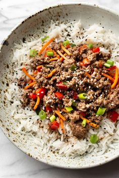 a white bowl filled with rice, meat and vegetables on top of a marble table