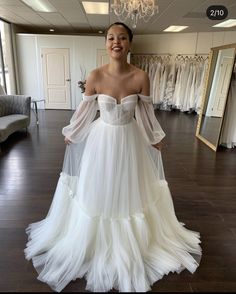 a woman in a white wedding dress standing in front of a mirror and looking at the camera