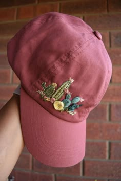 a person wearing a pink hat with cactus embroidered on the front and side, standing in front of a brick wall