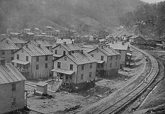 an old black and white photo of train tracks in the middle of town with houses on each side